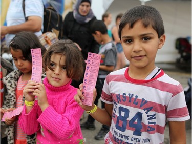 Syrian refugee children Layal, 5, and Mohamad, 8, right, line up for their ride tickets during their first Calgary Stampede in Calgary, Alta., on Wednesday July 13, 2016. Leah Hennel/Postmedia