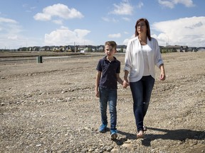 Monique Shaw and her son Luca Joint, 10, navigate rocky terrain near their home in the developing community of Sage Hill. Shaw is frustrated the Calgary Board of Education's two closest bus stops for the upcoming school year would have her son either walking on or near work sites like this or crossing the busy Symons Valley Road, which has no sidewalk on the east side.