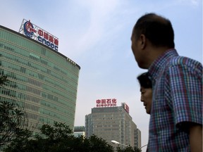 People walk past buildings of China's state-owned companies, China National Offshore Oil Corp. (CNOOC), left, and China Petroleum & Chemical Corp. (Sinopec), in Beijing.