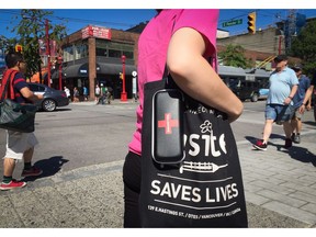 A woman carries a naloxone kit and a bag from Insite, the safe injection site, while walking in the Downtown Eastside of Vancouver, B.C., on Wednesday July 27, 2016. Naloxone is used to reverse the effects of overdoses in drug users who have taken opioids. The provincial government has announced the creation of a joint task force on overdose response. THE CANADIAN PRESS/Darryl Dyck ORG XMIT: VCRD111