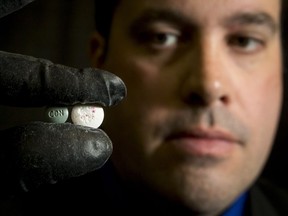 RCMP Cpl. Eric Boechler holds a green fake oxycodone pill containing fentanyl and a white demo pill laced with pink powder representing fentanyl to illustrate inconsistent mixing during a fentanyl processing demonstration.
