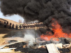 Tires burn as armed soldiers and law enforcement officers stand in formation to force pipeline protesters off private land in Morton County, N.D.