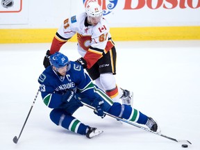 Vancouver Canucks' Henrik Sedin, bottom, of Sweden, moves the puck while being checked by Calgary Flames' Brett Kulak during the third period of a pre-season NHL hockey game in Vancouver, B.C., on Thursday October 6, 2016.