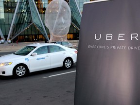 A taxi drives by a sign announcing the kickoff of Uber ride service in Calgary on Thursday, Oct. 15, 2015.