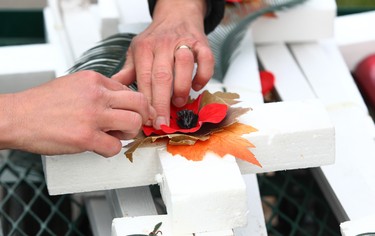 A volunteer decorates a cross with a poppy during the set-up at the Field of Crosses Memorial Project in Calgary, Alta on Saturday October 22, 2016 near Memorial Dr and Centre St NW. Starting November 1st to November 11th, over 3,200 crosses are being displayed on a 5 acre city park in military cemetery formation to memorialize southern Alberta soldiers who were killed in action.  Each cross is inscribed with the name, age at death, rank, regiment and date of death of a soldier who lost his or her life in a foreign land, fighting for the freedoms we all enjoy today. Jim Wells/Postmedia