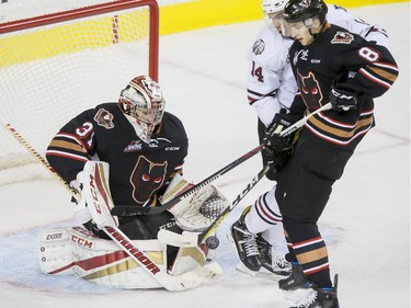 Austin Pratt of the Red Deer Rebels and Vladislav Yeryomenko of the Calgary Hitmen eye a puck in front of Hitmen goalie Cody Porter during WHL action at at the Scotiabank Saddledome in Calgary on ov. 22, 2016.