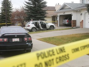 Calgary police officers inspect a white BMW parked in the driveway of a house at 196 Riverbend Drive SE in which a man was killed on Oct. 31, 2016.
