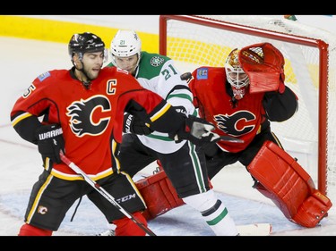Mark Giordano of the Calgary Flames and Antoine Roussel of the Dallas Stars tussle near an airborne puck in front of Flames goalie Brian Elliott during NHL action in Calgary, Alta., on Thursday, Nov. 10, 2016. Lyle Aspinall/Postmedia Network
