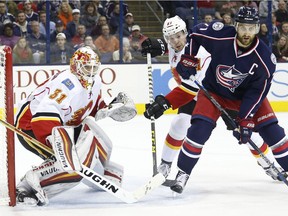 Calgary Flames' Chad Johnson, left, protects the net as teammate Brett Kulak, center, and Columbus Blue Jackets' Nick Foligno look for the puck during the second period of an NHL hockey game Wednesday, Nov. 23, 2016, in Columbus, Ohio.