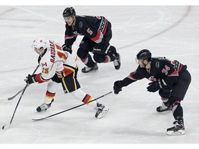Calgary Flames' Johnny Gaudreau (13) shoots and scores as Carolina Hurricanes' Noah Hanifin (5) and Phillip Di Giuseppe (34) defend during the third period of an NHL hockey game in Raleigh, N.C., Sunday, Feb. 26, 2017. Calgary won 3-1.