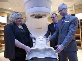 Sarah Hoffman, Minister of Health, left, Dr. Francois Belanger, middle, and Dr. Andrew Daly look at a patients mask on the radiation linear excelerator machine at theTom Baker Cancer Centre in Calgary, Alta., on Friday March 10, 2017. Leah Hennel/Postmedia