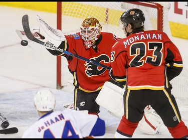Calgary Flames goalie Brian Elliott swats a puck near teammate Sean Monahan and near Calvin de Haan of the New York Islanders during NHL action in Calgary, Alta., on Sunday, March 5, 2017. The Flames were gunning for their seventh straight win. Lyle Aspinall/Postmedia Network