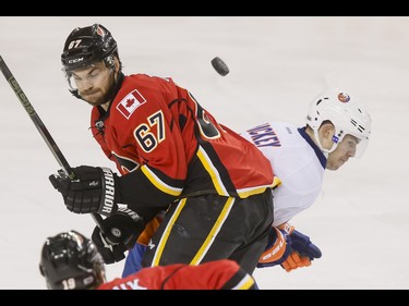 A puck sails between Michael Frolik of the Calgary Flames and Thomas Hickey of the New York Islanders during NHL action in Calgary, Alta., on Sunday, March 5, 2017. The Flames were gunning for their seventh straight win. Lyle Aspinall/Postmedia Network