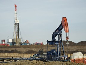 Pumpjack works in the foreground with a drilling rig on a Husky Oil site east of Bruderheim, Alberta