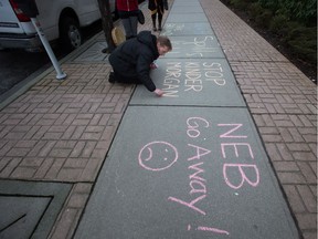 A woman writes a message in chalk during a protest outside National Energy Board hearings on the proposed Trans Mountain pipeline expansion in Burnaby, B.C., on Tuesday January 19, 2016. The proposed $5-billion expansion would nearly triple the capacity of the pipeline that carries crude oil from near Edmonton to the Vancouver area to be loaded on tankers and shipped overseas.