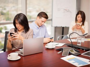 Hispanic people in a meeting room ignoring their work and doing some social networking on their smartphones