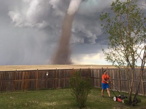 Theunis Wessels mows his lawn at his home in Three Hills as a tornado is seen in the background on Friday, June 2, 2017.