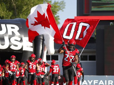 Stampeders DB Tunde Adeleke carries the Canadian flag onto the field before the Calgary Stampeders CFL season opener against the Ottawa Redblacks during CFL football in Calgary. The '00' Flag was carried in memory of the late, great Stampeders legend Sugarfoot Anderson who passed away in March at the age of 97. AL CHAREST/POSTMEDIA