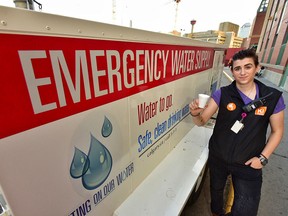 Adult care worker Mollie Grill-Donovan stands outside an emergency water wagon deployed at the Calgary Drop-In Centre on Saturday. The mobile water station was one of three deployed to homeless shelters by the city in response to the current heat wave.