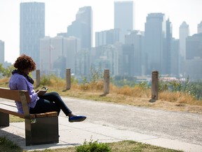 Grace Ndovi sits on a bench along Crescent Road NW overlooking the downtown skyline as people enjoy the 21 C weather despite smoky skies from wildfires in the Rocky Mountains on Friday, September 1, 2017 in Calgary, Alta. Britton Ledingham/Postmedia Network