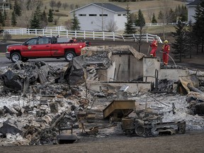 Firefighters monitor the remains of a house that was destroyed by grass fires near Airdrie on Wednesday, Oct. 18, 2017.
