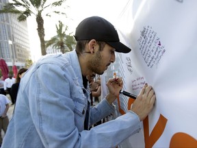 In this Tuesday, Oct. 3, 2017 photo, Norman Casiano, a survivor of the Pulse nightclub shooting, writes a note on a banner during a vigil in Orlando, Fla., to show solidarity with the victims of the mass shooting in Las Vegas. Casiano was hiding in a bathroom stall with dozens of others when the Orlando gunman shot him twice through the stall door. He's on disability and says he still has anxiety and post-traumatic stress. Las Vegas "was a big trigger. I still mustered up to come here, and to show the support we were shown last year," Casiano said. (AP Photo/John Raoux)