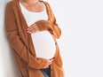 Beautiful pregnant woman touching her belly with hands on a white background. Young mother anticipation of the baby. Image of pregnancy and maternity. Close-up, copy space, indoors. Maternity wear
