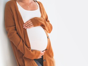 Beautiful pregnant woman touching her belly with hands on a white background. Young mother anticipation of the baby. Image of pregnancy and maternity. Close-up, copy space, indoors. Maternity wear