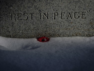 A poppy lies in the snow at the base of a veteran's grave marker during a Remembrance Day service in Calgary, Saturday, Nov. 11, 2017.