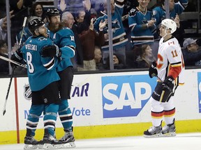 San Jose Sharks' Joe Pavelski (left) celebrates his goal with teammate Joe Thornton, center, while Calgary Flames' Mikael Backlund (11) skates past during the first period of an NHL hockey game Thursday, Dec. 28, 2017, in San Jose, Calif.