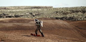 A crew member hikes up a hill and takes magnetic readings near the Mars Desert Research Station.