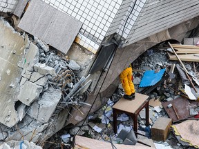 TOPSHOT - A rescue worker clears debris to make way for the recovery of the dead bodies of a Hong Kong Canadian couple from the Yun Tsui building, which is leaning at a precarious angle, in the Taiwanese city of Hualien on February 9, 2018, after the city was hit by a 6.4-magnitude quake late on February 6. After hours of painstaking search efforts, Taiwanese rescue workers pulled two more bodies from the flattened remains of a hotel February 9, bringing the death toll from a deadly 6.4-magnitude quake to 12.  / AFP PHOTO / Anthony WALLACEANTHONY WALLACE/AFP/Getty Images