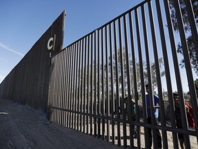 In this March 5, 2018, photo, boys look through an older section of the border structure from Mexicali, Mexico, alongside a newly-constructed, taller section, left, in Calexico, Calif.