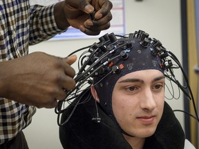 University of Calgary bio-medical engineering student Ibukun Oni adjusts a head cap worn by Carter Randall which can detect and monitor concussions.