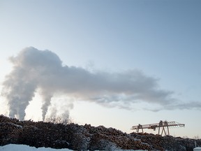 A lumber mill owned and operated by Millar Western is pictured exhausting steam, while a massive cranes moves bundles of lumber on a cold afternoon, in front of it are stacks of trees waiting to be cut and shipped on Thursday December 18, 2014 in Whitecourt, Alta. Adam Dietrich/Whitecourt Star/QMI Agency