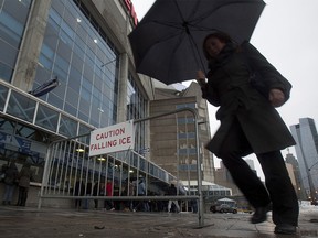 Pedestrians walk by barrier with warning sign outside Roger's Centre in Toronto on Monday April 16, 2018. The Blue Jays American League MLB baseball game against the Kansas City Royals was cancelled over safety concerns from ice falling from the CN tower. THE CANADIAN PRESS/Fred Thornhill ORG XMIT: FJT304