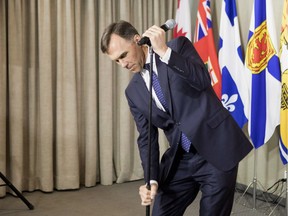 Federal Finance Minister Bill Morneau adjusts the height of a microphone stand before updating the media on the talks involving the plans for Trans Mountain pipeline extension during a briefing in Toronto on Wednesday, April, 11, 2018.