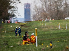 Two workers talk as flags mark an underground pipeline location as work continues at Kinder Morgan's facility in preparation for the expansion of the Trans Mountain Pipeline, in Burnaby, B.C., on April 9, 2018.