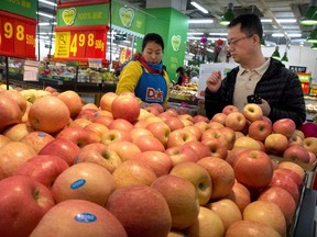 FILE - In this March 23, 2018, file photo, a woman wearing a uniform with the logo of an American produce company helps a customer shop for apples a supermarket in Beijing. China raised import duties on a $3 billion list of U.S. pork, fruit and other products Monday, April 2, 2018 in an escalating tariff dispute with President Donald Trump that companies worry might depress global commerce.
