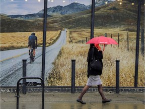 A pedestrian passes by a mural of the Rocky Mountains as a rain shower falls in  Calgary, Alta., Tuesday, May 2, 2017. Forecasts for the Calgary area are calling for temperatures in the +20C range the rest of the week.