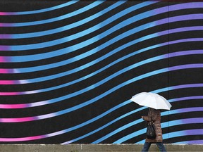 A pedestrian takes cover under an umbrella while walking along 61 Ave SW in Calgary on Tuesday, October 31, 2017. Jim Wells/Postmedia