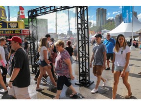 People move through the mister as they throng the midway at the Calgary Stampede in Calgary, Ab., on Friday July 13, 2018. Mike Drew/Postmedia