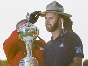 Dustin Johnson of the United States hoists the Canadian Open championship trophy as a Royal Canadian Mounted Police officer places his Stetson on his head at the Glen Abbey Golf Club in Oakville Ont., on Sunday.