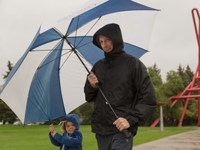 Abygail Schneider, 2, helps her father Ted with carrying a big umbrella through the rain at the University of Calgary, in Calgary on Friday, Aug. 21, 2015.