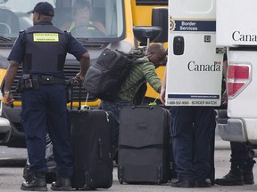 A second federal probe is underway in Prince Edward Island alleging hundreds of people gained permanent residency in Canada by using local addresses where they didn't live, under a provincial business immigration system that's faced criticism for loose oversight. A man removes his belongings from a CBSA truck at a processing centre for asylum seekers at the Canada-United States border in Lacolle, Que. Thursday, August 10, 2017.