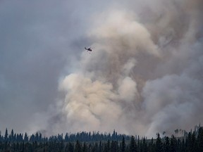A helicopter flies past a plume of smoke rising from a wildfire near Fraser Lake, B.C., on Wednesday Aug. 15, 2018.