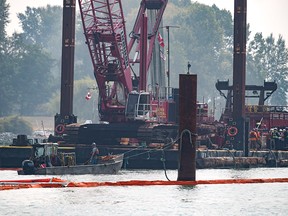 Workers stand on a small boat as a diver works below them after a tugboat capsized and sank on the Fraser River between Vancouver and Richmond, B.C., on Tuesday Aug. 14, 2018. 
Four people aboard the vessel were all rescued.