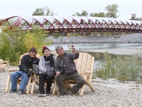 Manny Pabuquibot  takes a smartphone photo with his parents Sabas and Luz Pabquibot in the newly opened park area in West Eau Claire Park in Calgary on Friday, September 21, 2018. The iconic Peace Bridge is in the background. Jim Wells/Postmedia