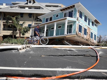 MEXICO BEACH, FL - OCTOBER 11:  Tom Bailey walks his bike past a home that was carried across a road and slammed up against a condo complex as Hurricane Michael passed through the area on October 11, 2018 in Mexico Beach, Florida.  The hurricane hit the panhandle area with category 4 winds causing major damage.  (Photo by Joe Raedle/Getty Images)