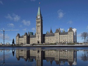 The centre block of the Parliament buildings is reflected in a puddle as a woman walks past, in Ottawa on February 1, 2016. Canada can be fixed, says columnist Rob Breakenridge.